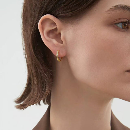 Close-up of model wearing gold twist huggie hoop earrings
