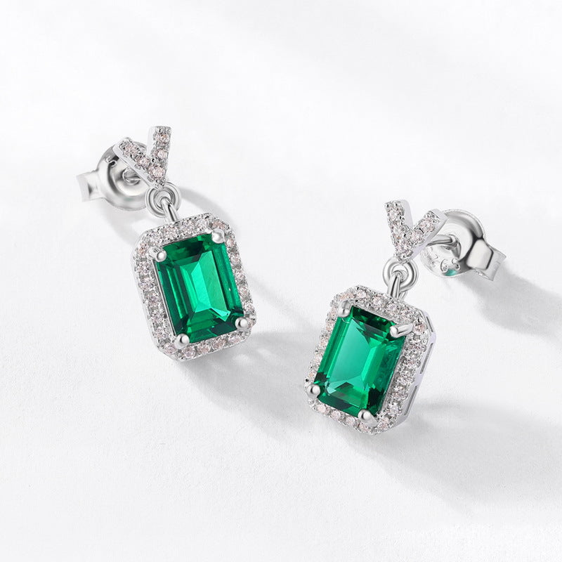 Sterling silver emerald cut drop earrings with green gemstone and diamond halo, modern minimalist design, Aeterna Jewelry flat lay photo