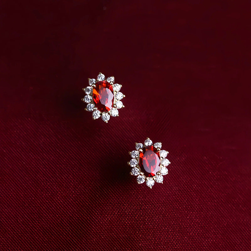 Elegant garnet halo stud earrings displayed on deep red fabric background