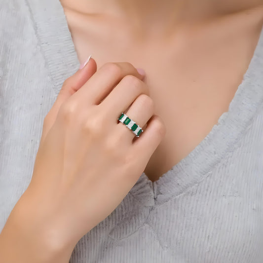 Model wearing Aeterna Jewelry emerald cut eternity band ring, close-up hand view showing alternating green and white baguette stones in elegant silver setting