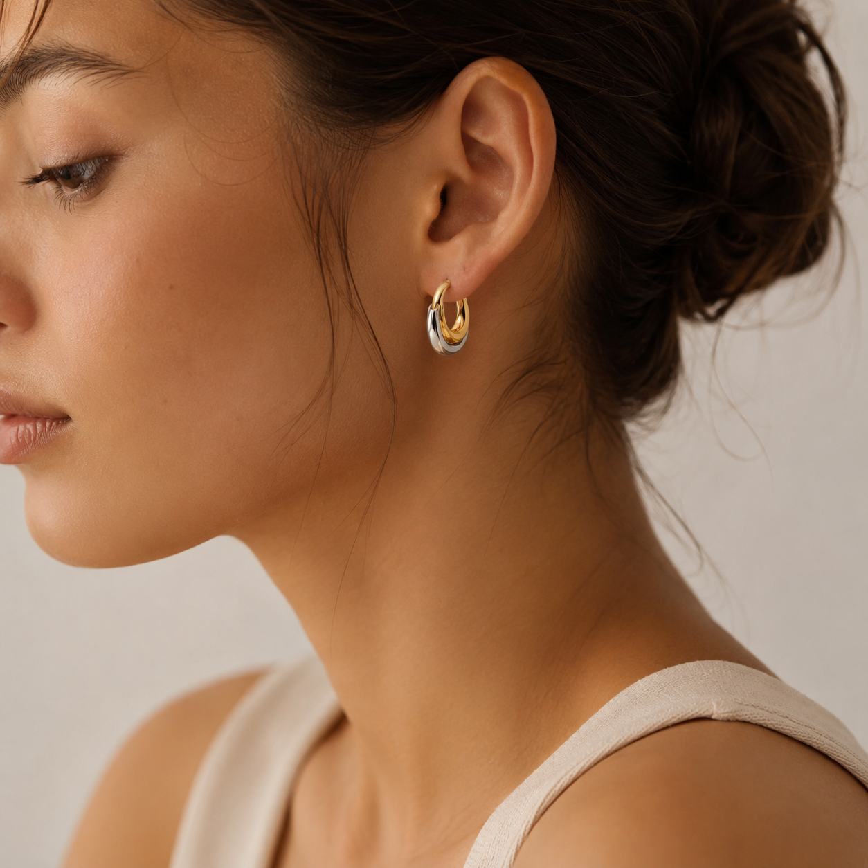 Side profile of woman wearing sculpted two-tone hoop earrings in a minimal, modern styling shot