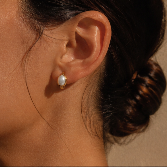 Gold pearl huggie earrings worn on model ear in warm close-up