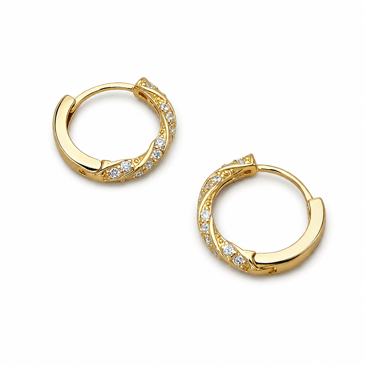 Angled view of gold twist pavé huggie hoop earrings on white background