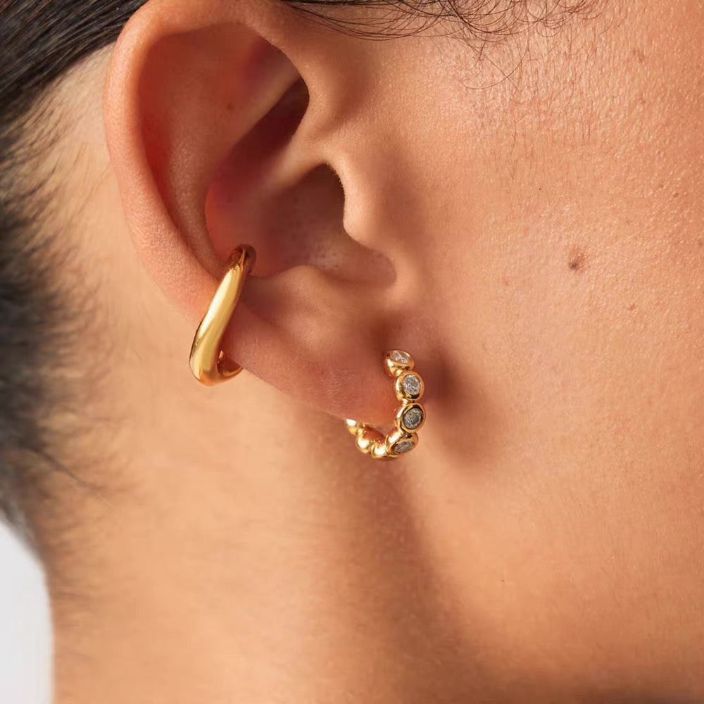 Close-up of gold Elara bezel huggie earrings worn in a modern stacked ear look