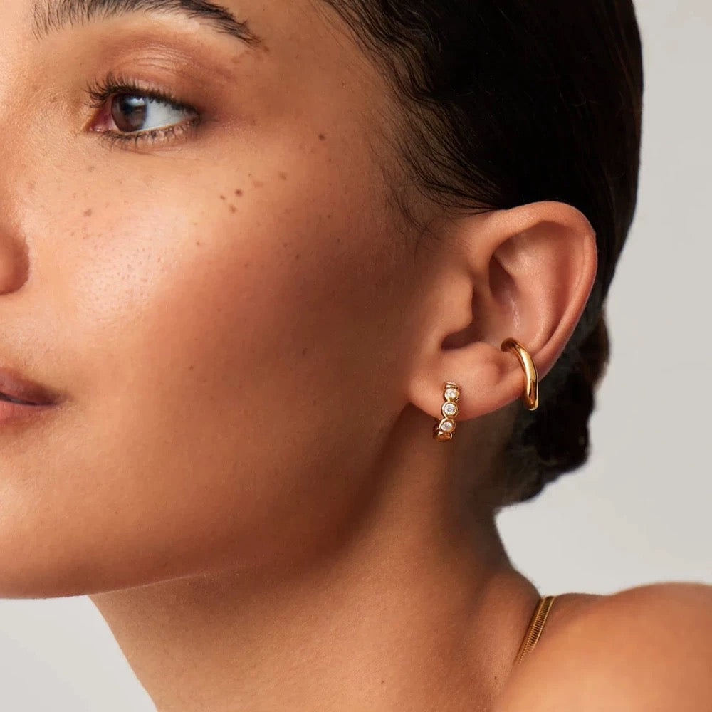 Model wearing gold bezel huggie earrings styled with a polished gold ear cuff