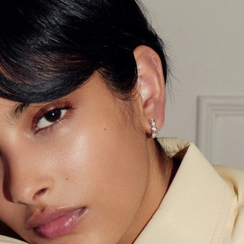 Model wearing silver Elara bezel huggie earrings with a tailored cream jacket