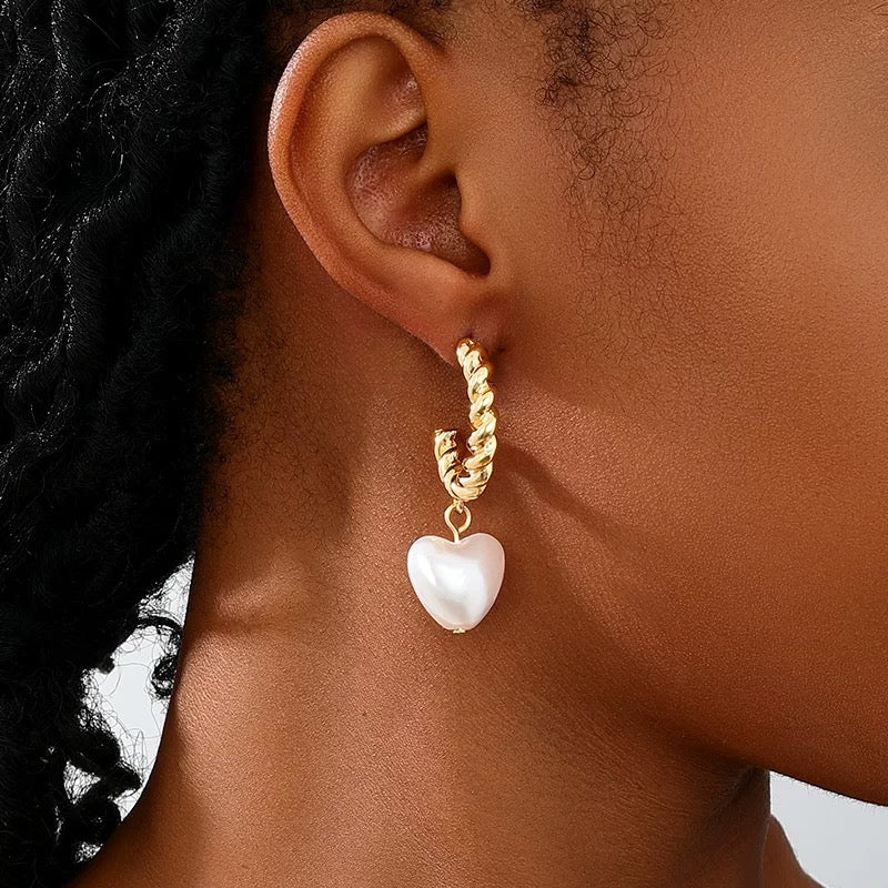 Model wearing gold twisted hoop earrings with heart-shaped pearl drop charm
