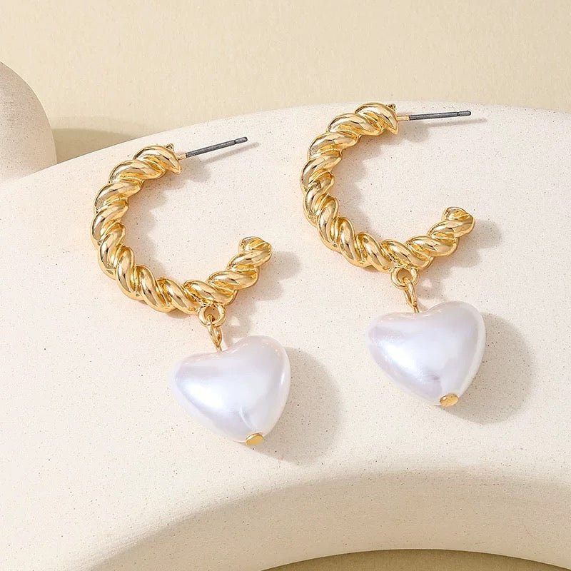 Close-up product photo of twisted gold hoop earrings with glossy heart-shaped pearl drops