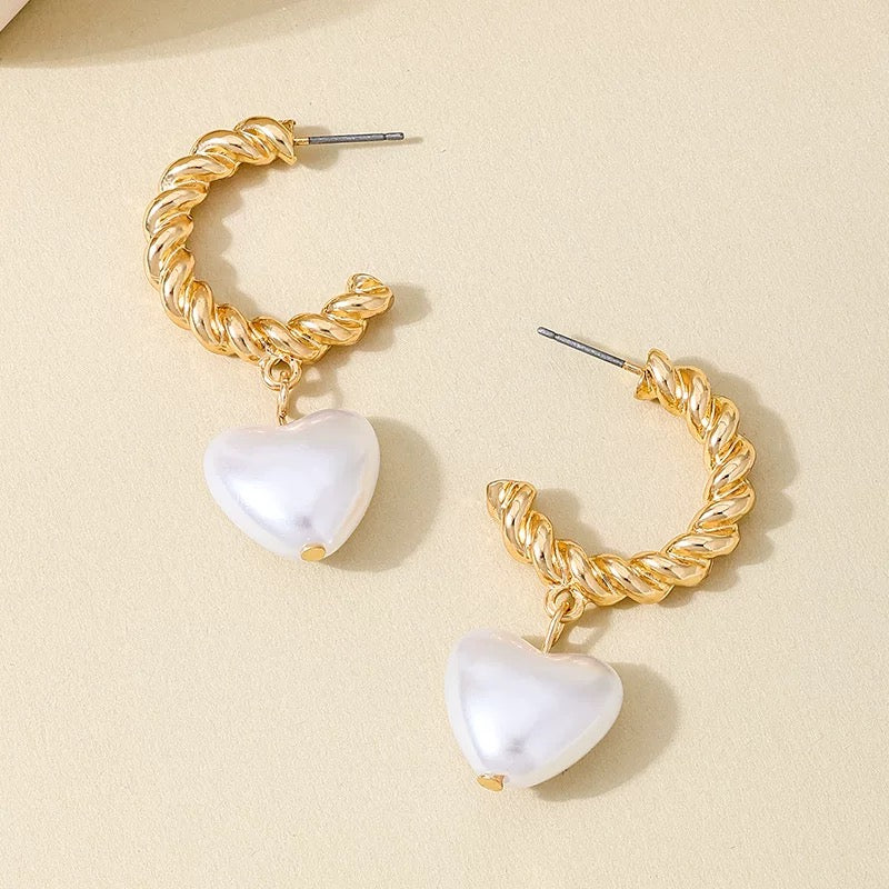 Gold pearl heart drop hoop earrings displayed on a soft beige background