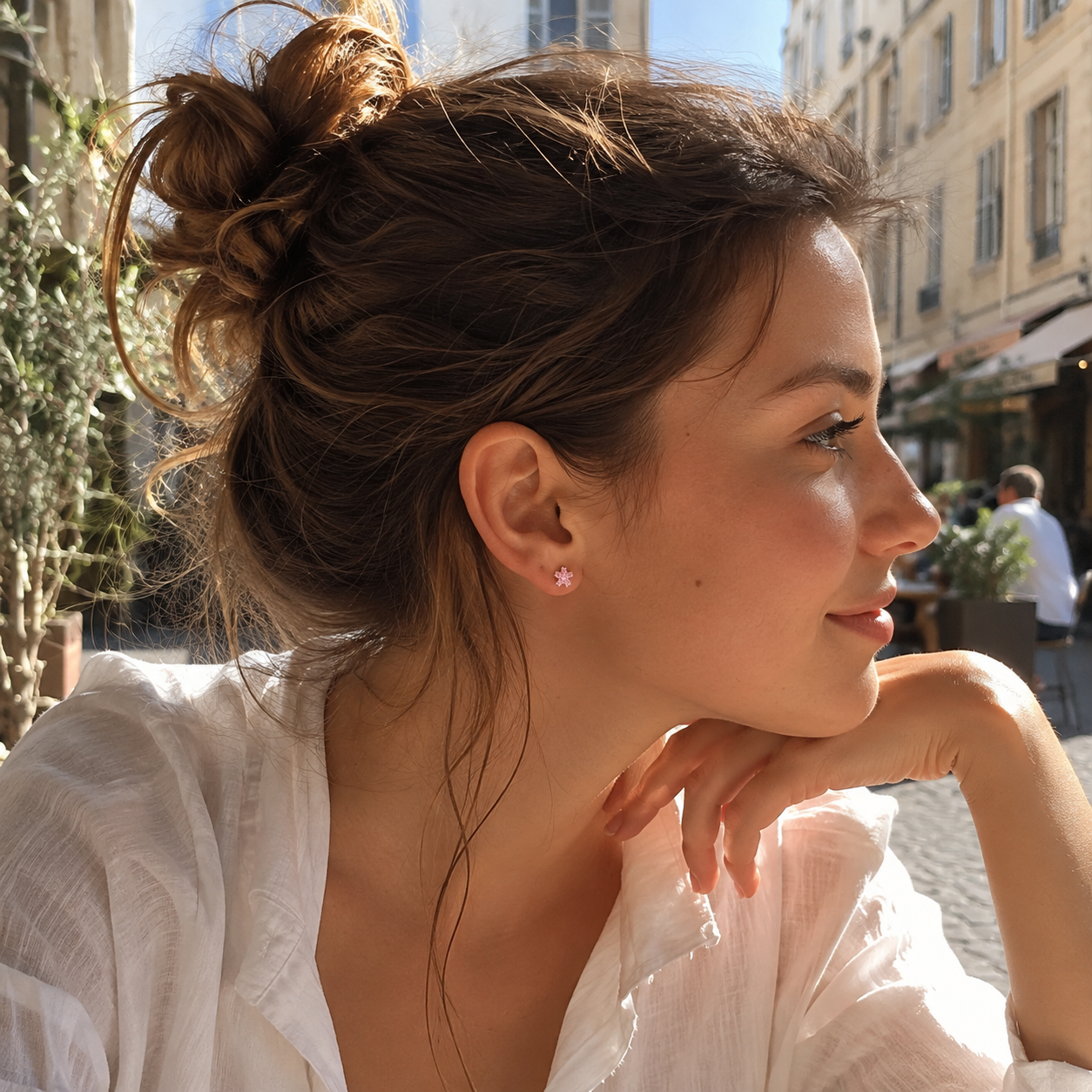 Model wearing a pink cubic zirconia blossom stud earring at an outdoor café