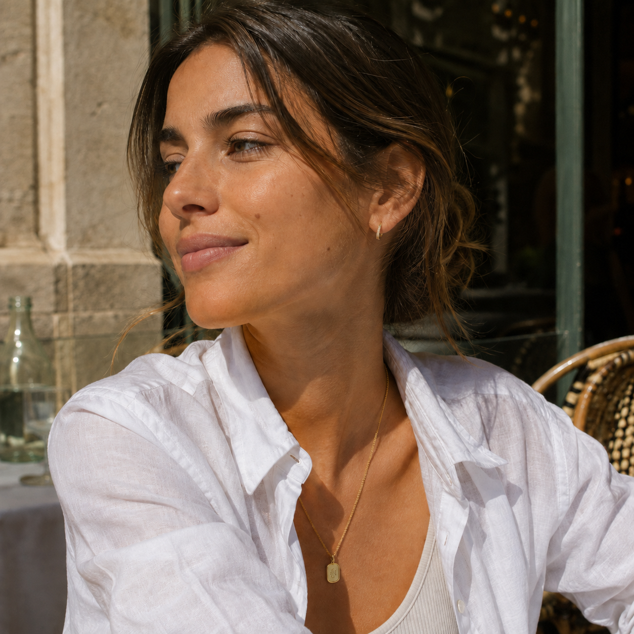 Model wearing gold Celeste mini pavé huggie earrings at an outdoor café