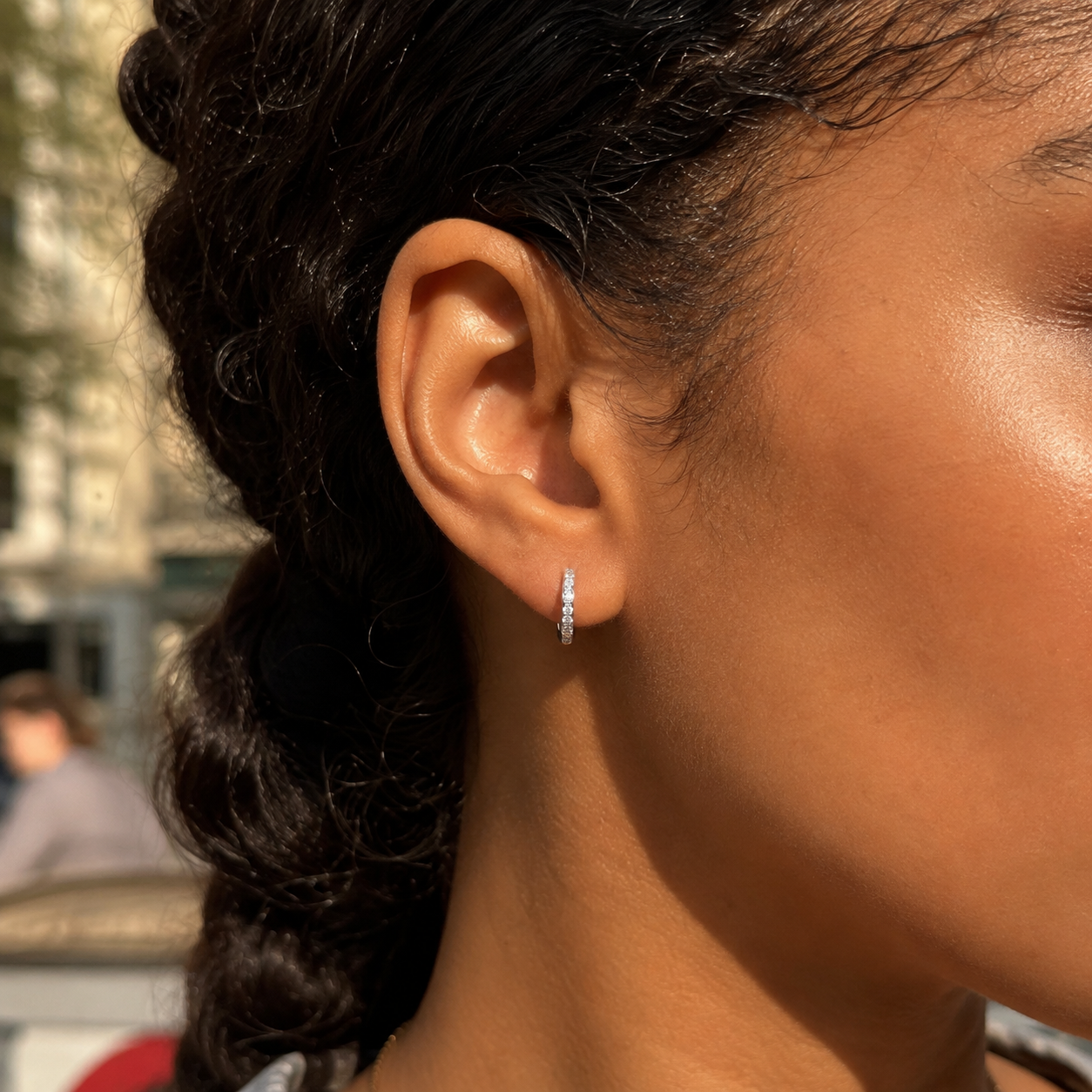 Close-up of silver Celeste mini pavé huggie earring worn outdoors