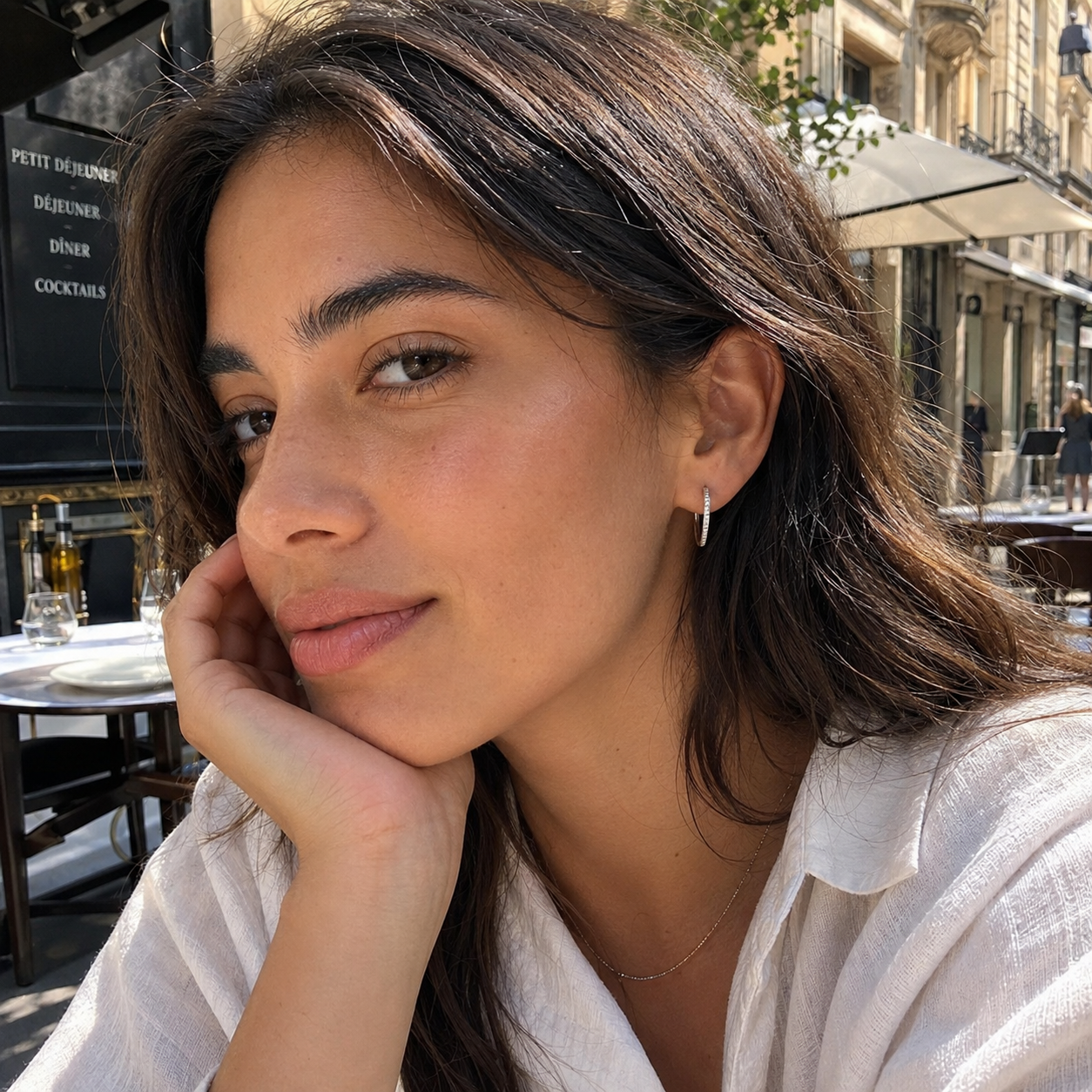 Model wearing silver Aurelia pavé hoop earrings at a sunlit outdoor café