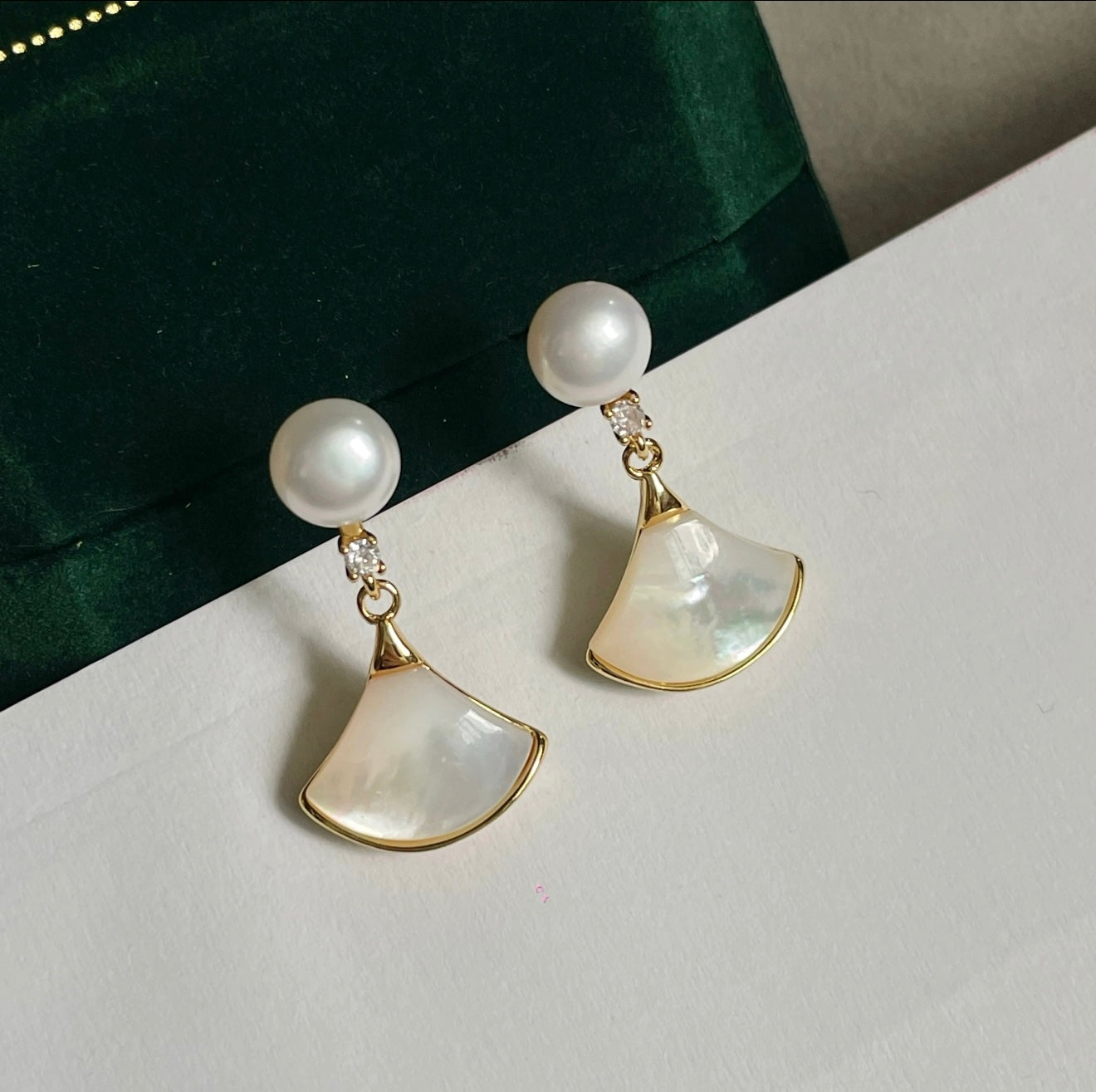 Gold pearl fan drop earrings displayed on a white and green background