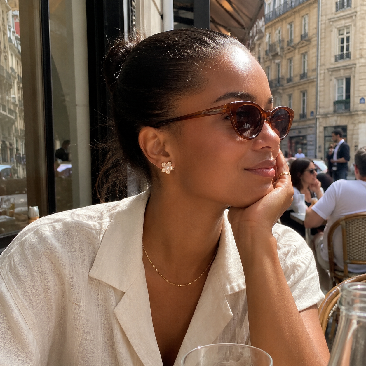 Model wearing gold pearl flower stud earrings at a European outdoor café
