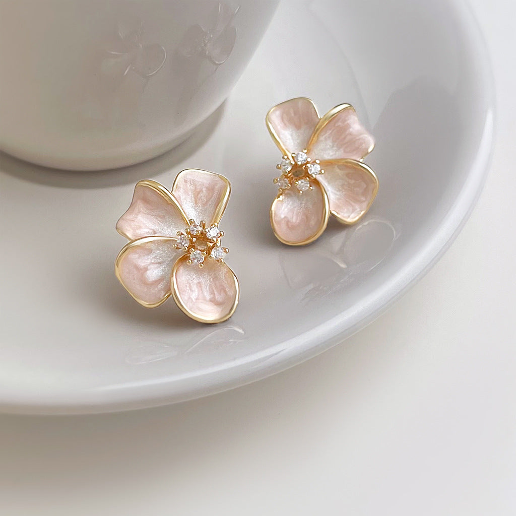 Pair of Rosalie Pink Blossom Stud Earrings with pearlescent pink petals and gold-tone edges on a white ceramic dish