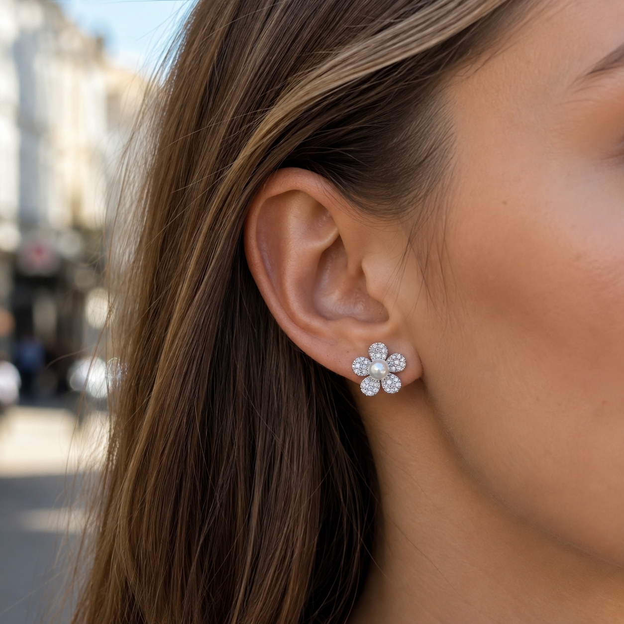 Close-up of Marielle Pearl Flower Stud Earrings worn on the ear against a blurred street background