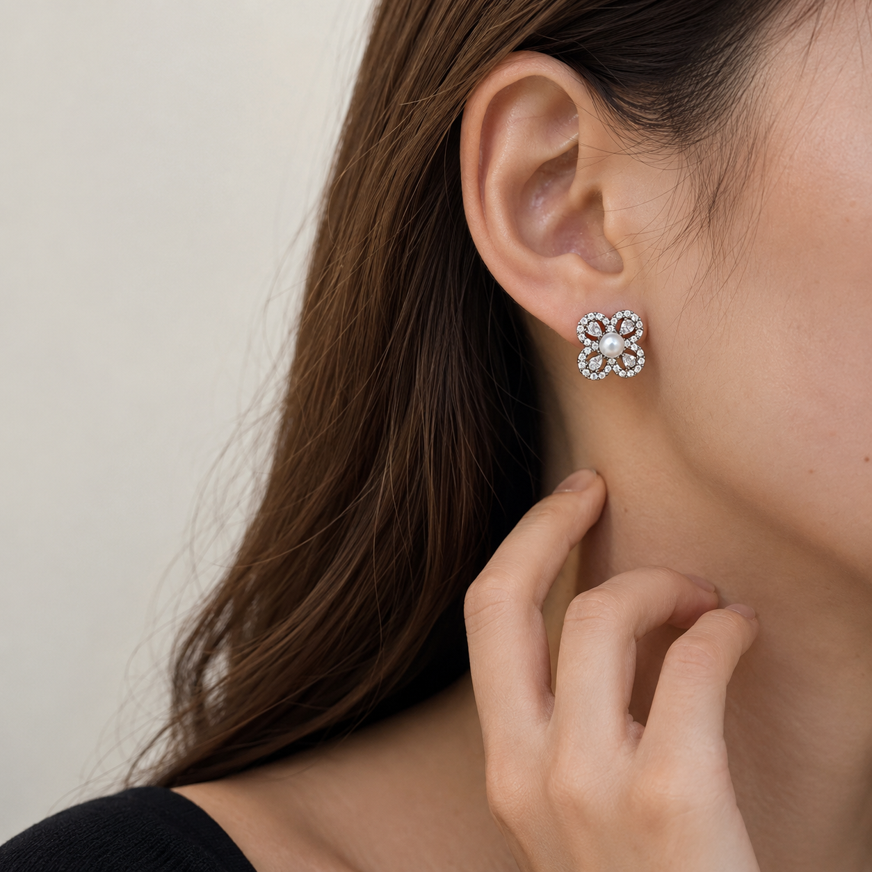 Close-up of Aurelia Pearl Clover Stud Earrings worn on the ear with a hand resting near the neck