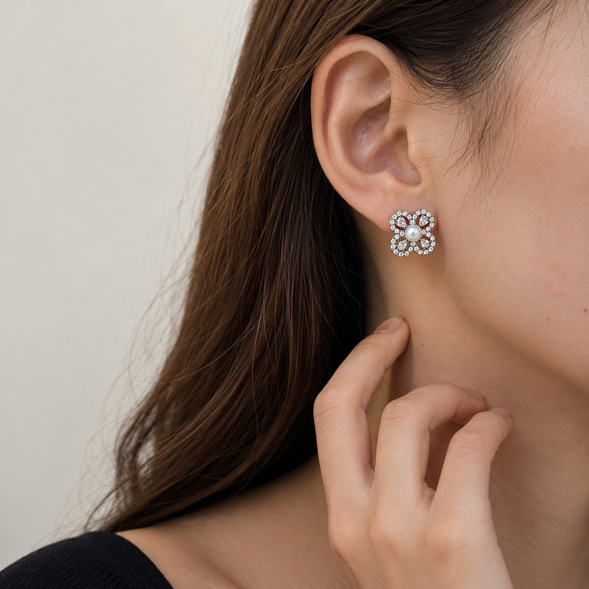 Close-up of Aurelia Pearl Clover Stud Earrings worn on the ear with a hand resting near the neck