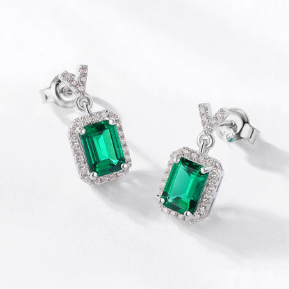 Sterling silver emerald cut drop earrings with green gemstone and diamond halo, modern minimalist design, Aeterna Jewelry flat lay photo
