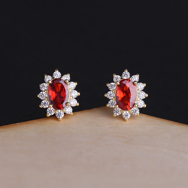 Close-up of garnet birthstone stud earrings with diamond-style halo on black background