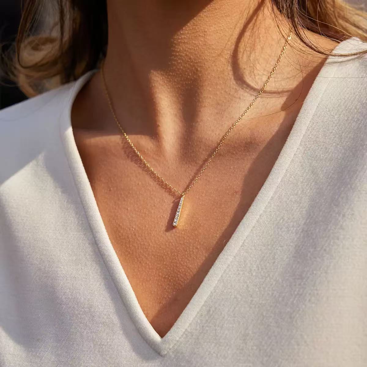 Gold pavé bar pendant necklace styled with a white V-neck outfit in sunlight