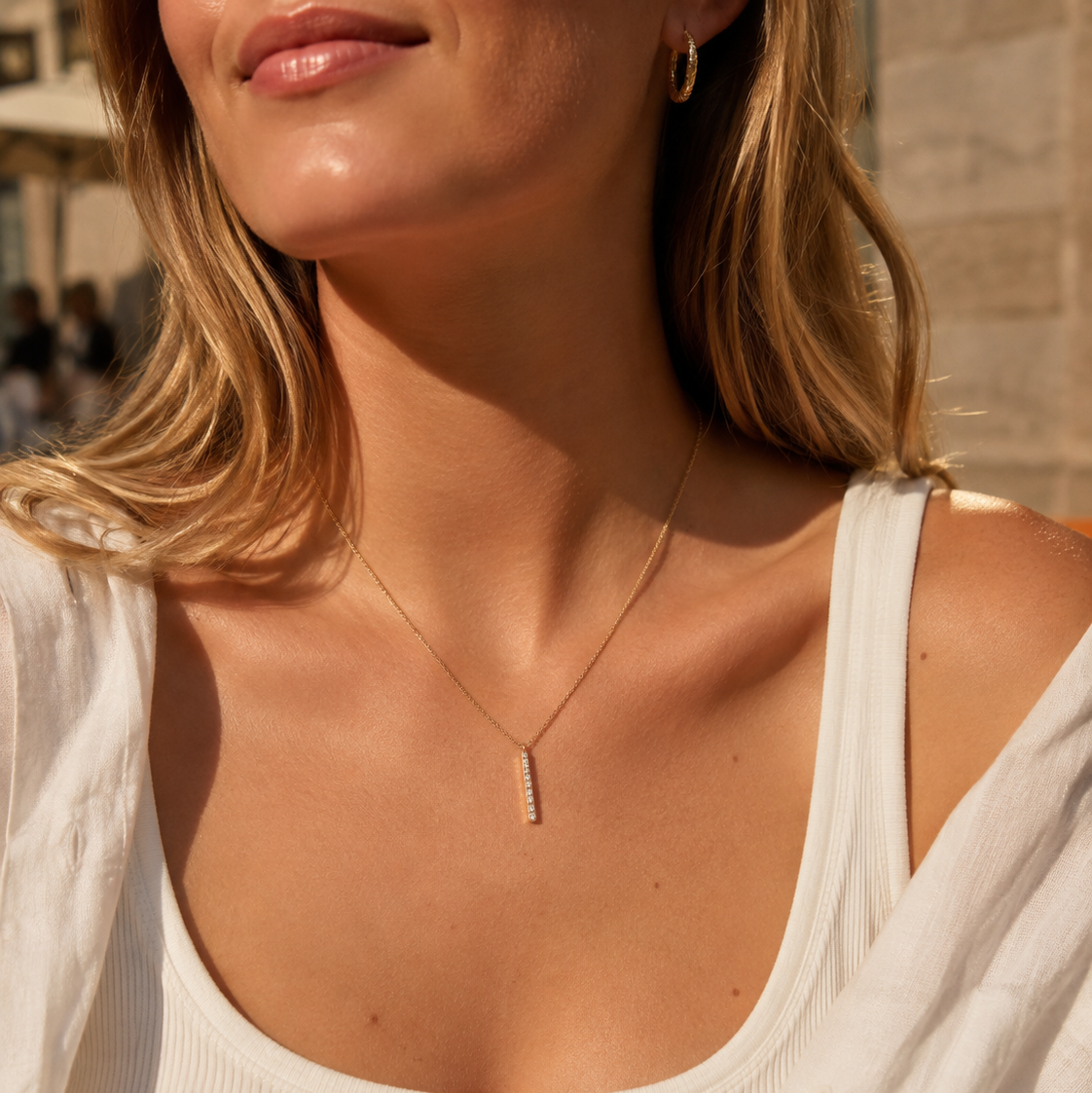 Close-up of gold cubic zirconia bar necklace worn with a white summer top