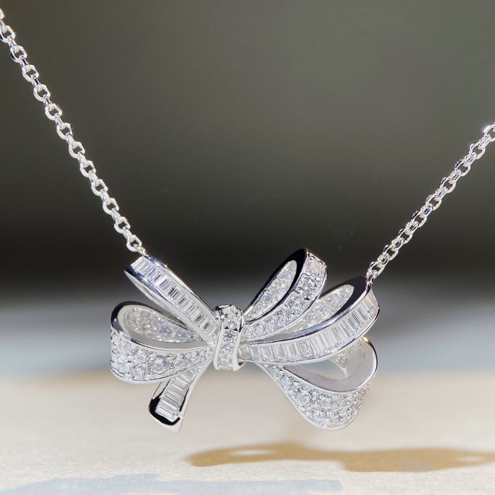 Close-up of diamond bow pendant necklace by Aeterna Jewelry, silver chain and baguette-cut stones sparkling under soft light